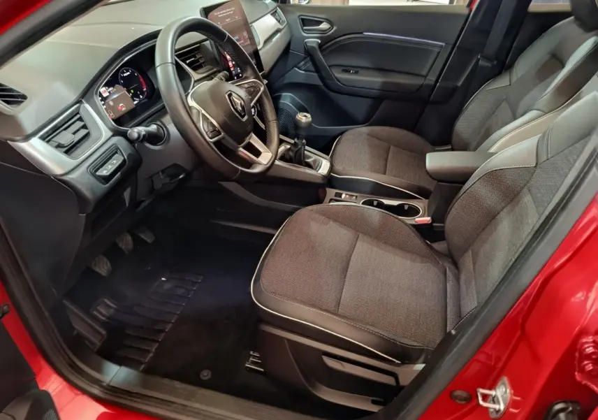 Vue intérieure côté conducteur du Renault Captur rouge 2024, montrant tableau de bord et sièges tissu gris.