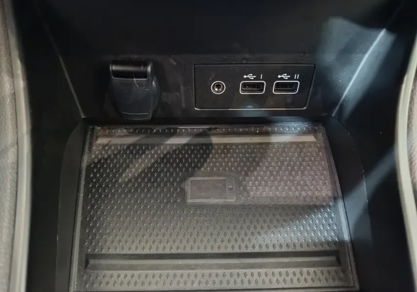 Gros plan sur la zone de recharge par induction et les ports USB noirs dans le compartiment central du Renault Captur rouge 2024.