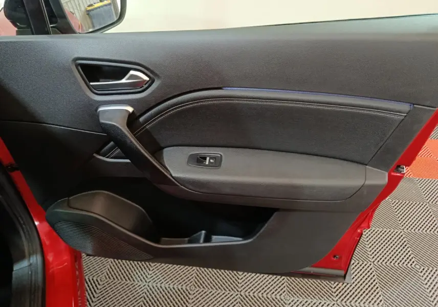 Vue intérieure de la porte avant gauche rouge du Renault Captur 2024 avec poignée et commande de vitre noire.