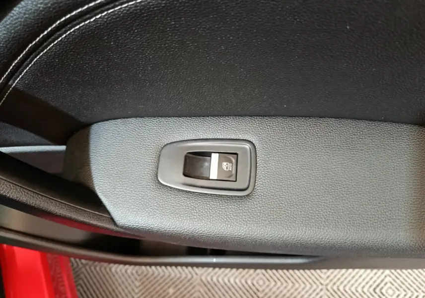 Détail de la commande de lève-vitre sur la porte intérieure noire du Renault Captur rouge 2024, côté conducteur.