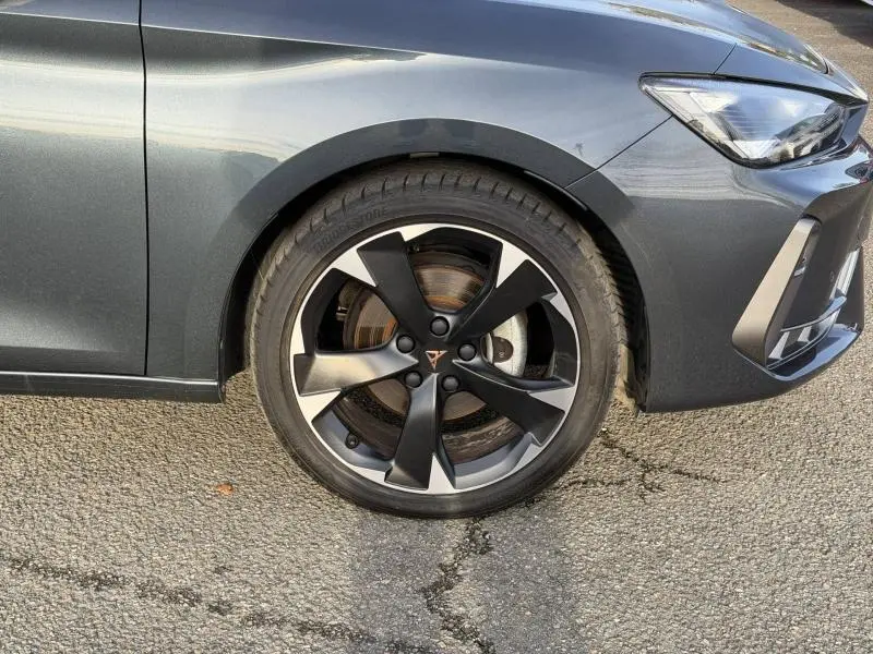 Gros plan sur la roue avant droite d’une SEAT LEON 1.5 eTSI Hybrid 2025 en gris magnétique métallisé avec jante noire et argentée.
