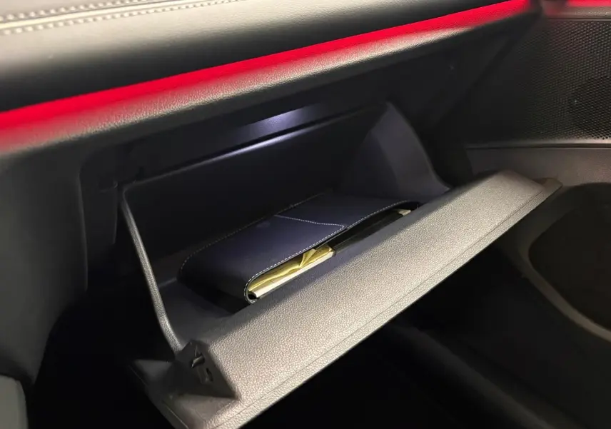 Gros plan sur la boîte à gants ouverte du Volkswagen Tiguan 2025, intérieur noir avec éclairage d'ambiance rouge.