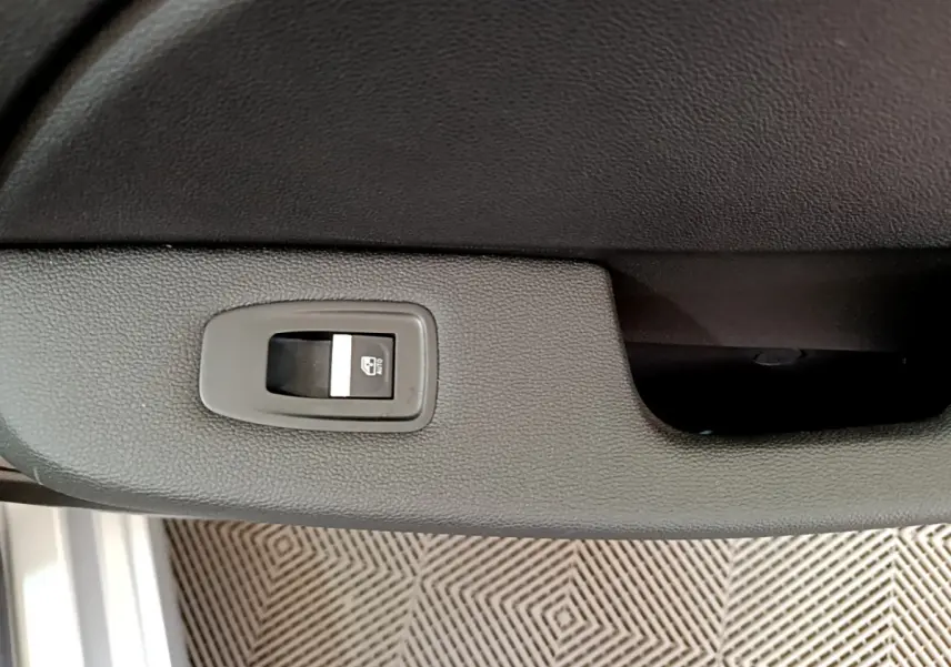 Gros plan sur le bouton de commande de lève-vitre sur la porte intérieure d’une Renault Clio Business gris clair.