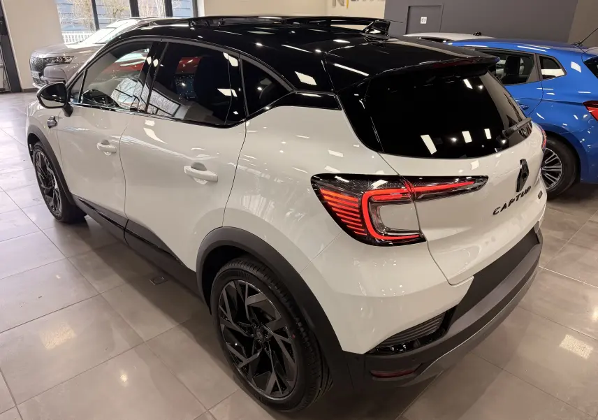 Vue 3/4 arrière droite du Renault Captur E-Tech blanc nacré avec toit noir et jantes noires en concession.