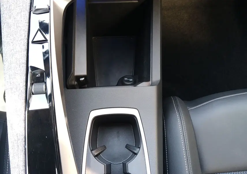 Vue plongeante sur la console centrale noire du Peugeot 3008 Hybrid 136 Allure 2024, avec porte-gobelets et commandes tactiles.