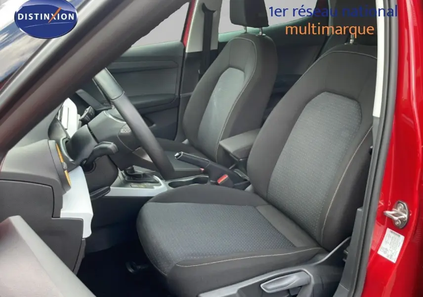Vue intérieure côté conducteur du SEAT Arona rouge désir métal, montrant les sièges en tissu noir et le volant multifonction.