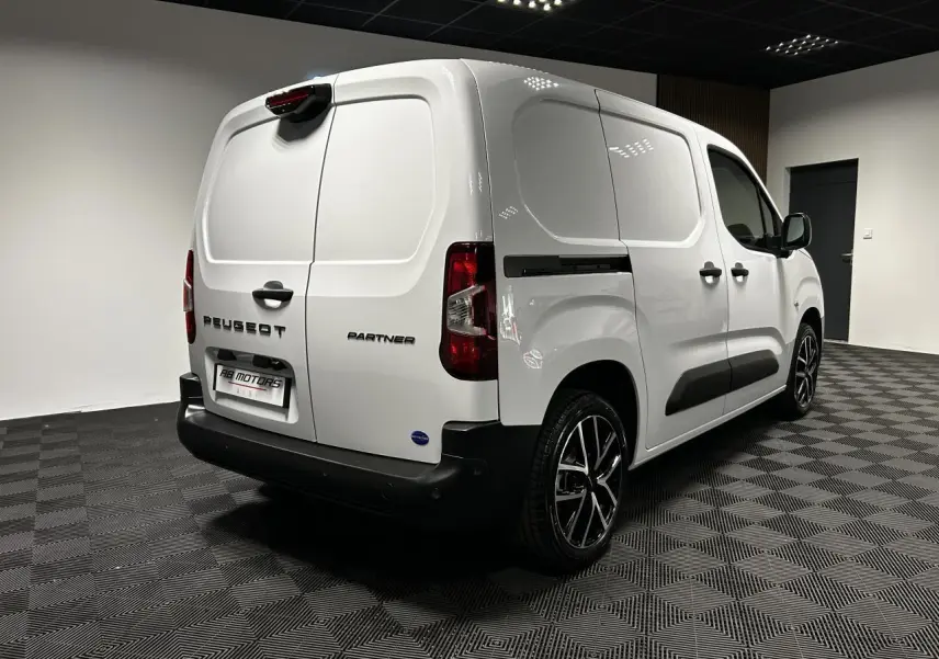 Vue 3/4 arrière droite du Peugeot Partner blanc Banquise avec jantes alu 17 pouces dans un showroom.
