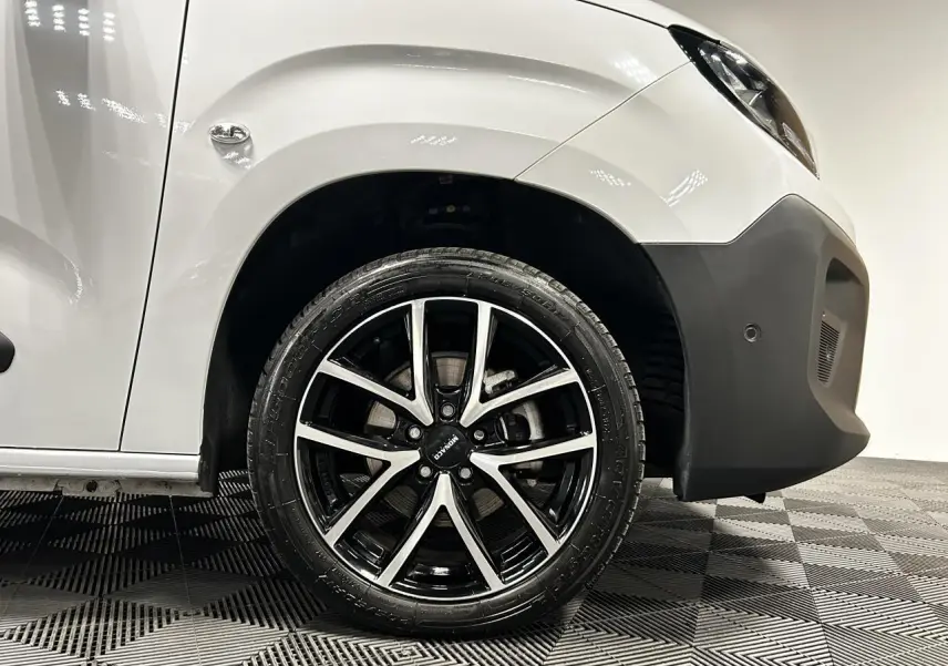 Gros plan sur la roue avant droite avec jante alu 17 pouces du Peugeot Partner blanc Banquise, partie avant visible.