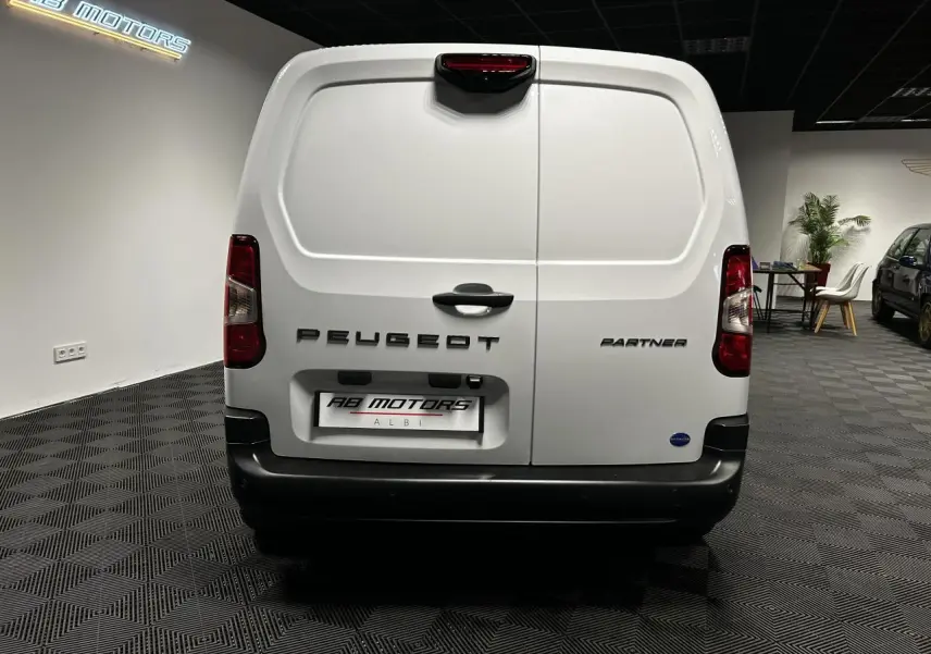 Vue arrière du Peugeot Partner blanc banquise 2025 avec portes battantes et pare-chocs noir dans un showroom.