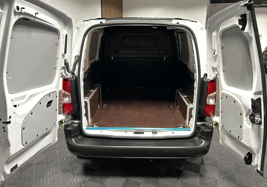 Vue arrière du Peugeot Partner blanc banquise 2025 avec portes battantes ouvertes et plancher de chargement en bois.