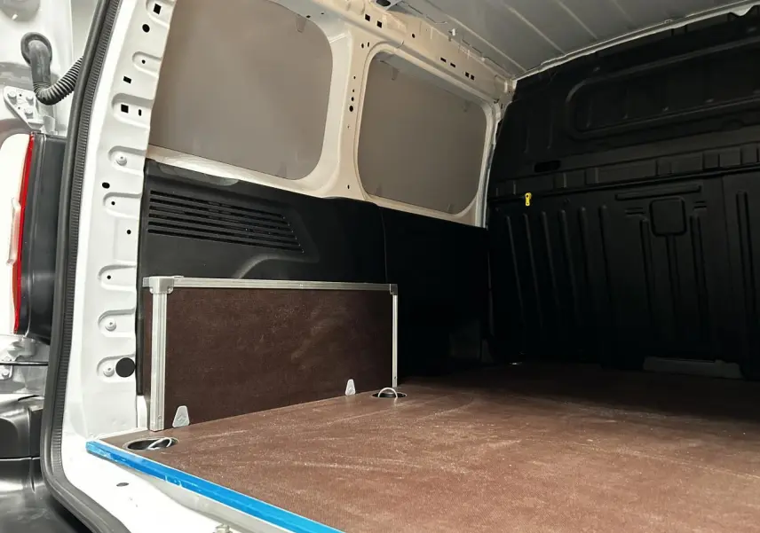 Vue intérieure arrière du Peugeot Partner blanc Banquise, plancher bois antidérapant avec anneaux d’arrimage visibles.