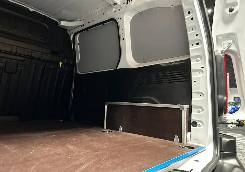 Vue intérieure arrière du Peugeot Partner blanc Banquise, montrant la zone de chargement avec plancher bois antidérapant et anneaux d’arrimage.