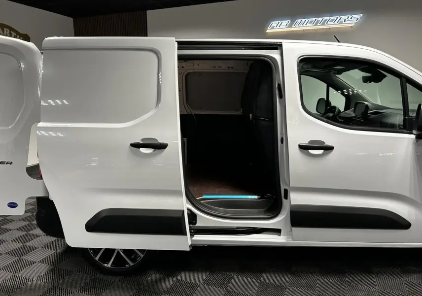 Vue latérale droite d’un Peugeot Partner blanc Banquise avec porte coulissante ouverte montrant l’espace de chargement.