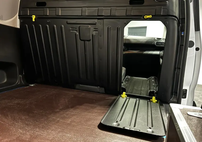Vue intérieure du coffre du Peugeot Partner blanc banquise 2025, avec cloison noire et plancher bois antidérapant.