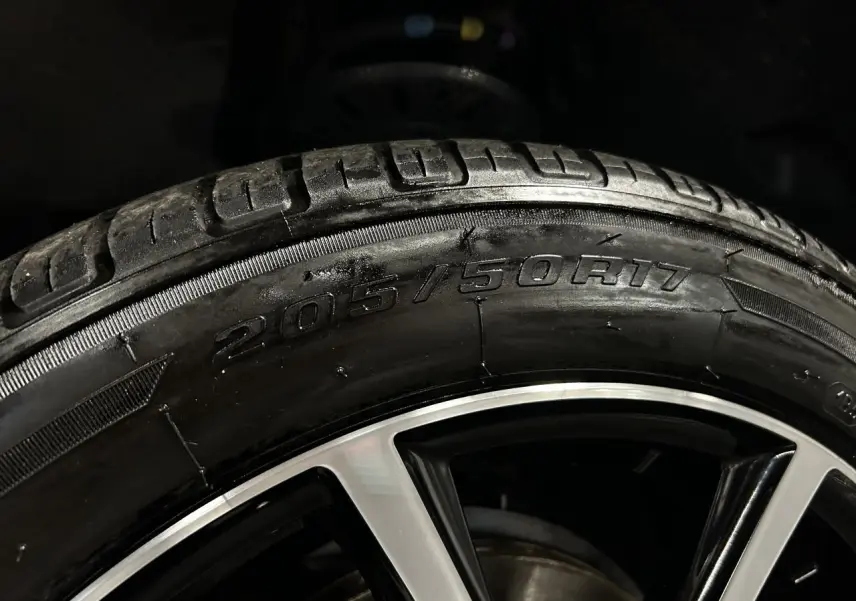 Gros plan sur la jante alu 17 pouces et le pneu 205/50R17 du Peugeot Partner blanc banquise, éclairage sombre.