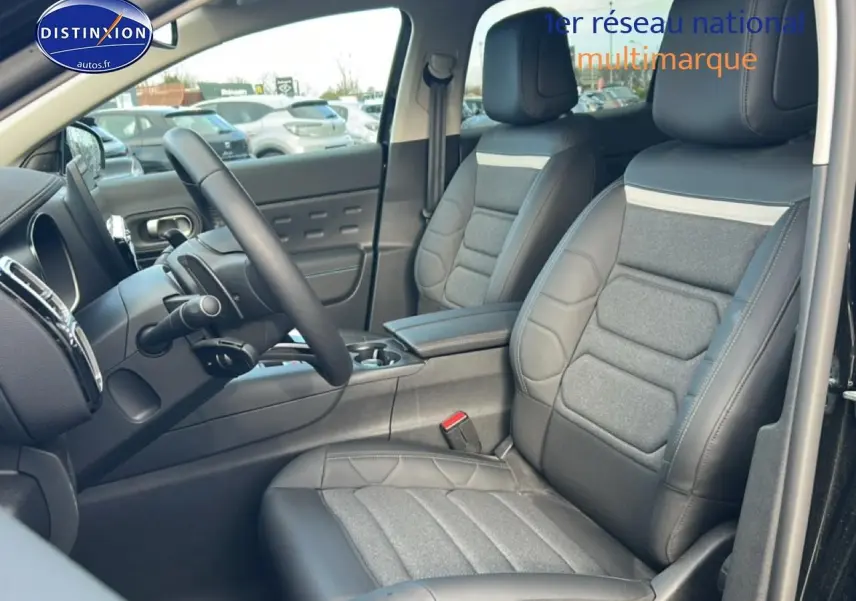 Vue intérieure côté conducteur du Citroën C5 Aircross 2025 noir, mettant en valeur les sièges cuir et tissu avec accoudoir central.