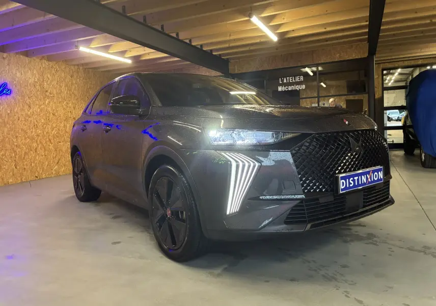 DS7 E-TENSE gris vue 3/4 avant gauche, phares LED allumés et calandre noire distinctive dans un atelier.