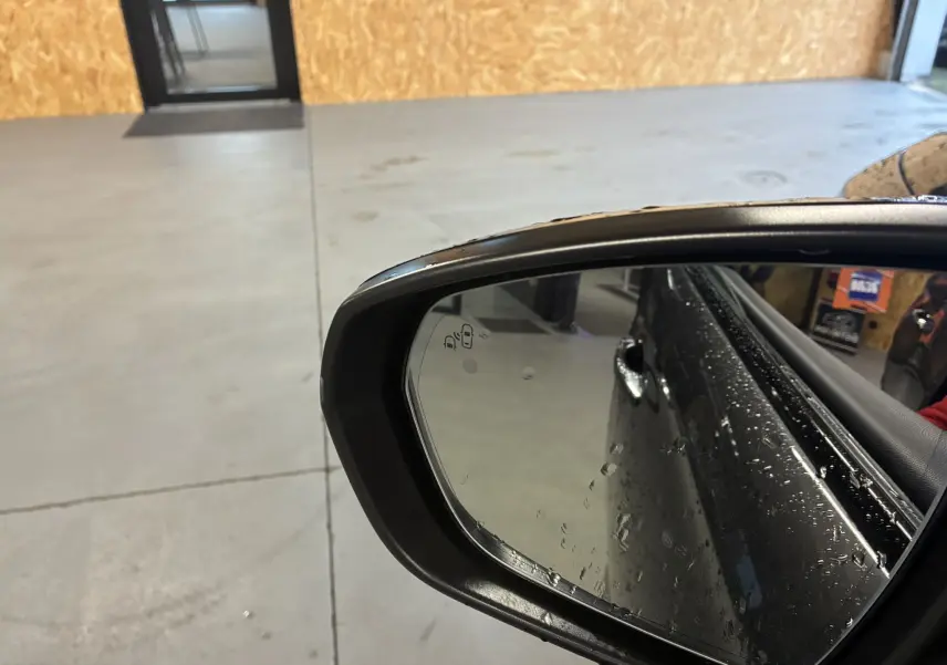 Rétroviseur côté droit du DS7 E-TENSE gris 2024 avec gouttes d'eau et reflet partiel de la porte arrière.