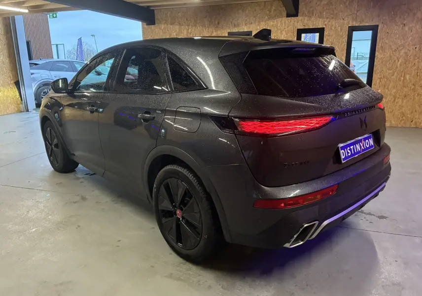 Vue 3/4 arrière droite du DS7 E-TENSE gris métallisé avec feux arrière LED allumés dans un garage.