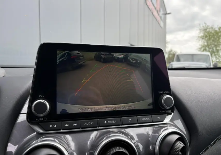Écran central du Nissan Juke blanc perle 2024 montrant la caméra de recul avec lignes d'aide au stationnement.