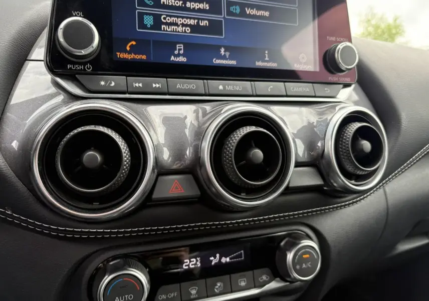 Détail du tableau de bord du Nissan Juke 2024 blanc perle, montrant les aérateurs ronds et l'écran tactile multimédia.