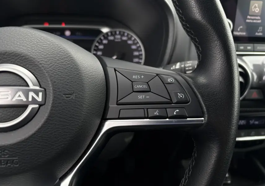 Gros plan sur le volant noir du Nissan Juke 2024 avec commandes de régulateur de vitesse et téléphone intégrées.
