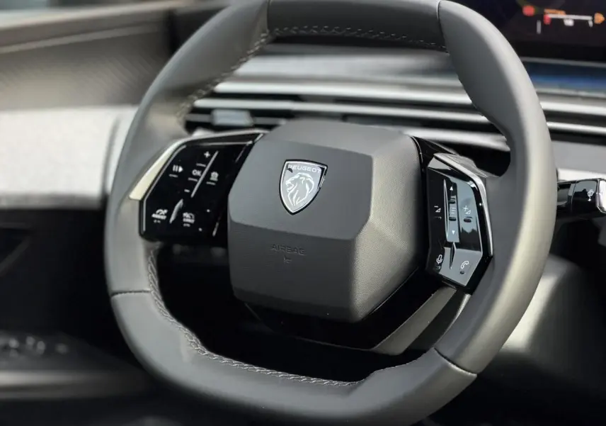 Gros plan sur le volant compact en cuir gris du Peugeot 3008 Hybrid 2025 avec commandes intégrées noir laqué.