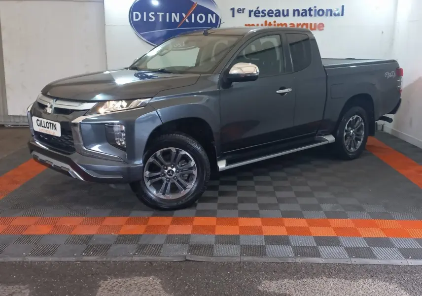 Mitsubishi L200 gris foncé en 3/4 avant droit, avec benne pick-up et jantes alliage visibles en intérieur showroom.
