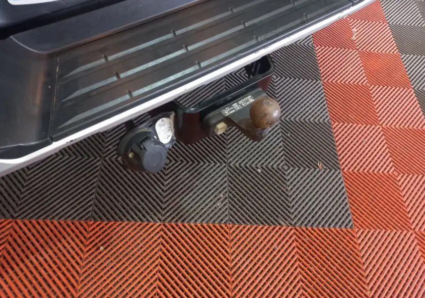 Gros plan sur l'attelage et la prise électrique arrière d'un Mitsubishi L200 gris foncé, vue du dessous du pare-chocs.