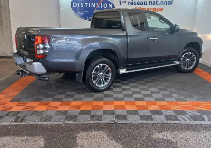 Vue latérale droite d’un pick-up Mitsubishi L200 gris foncé avec benne, jantes alliage et logo 4x4 visible à l’arrière.