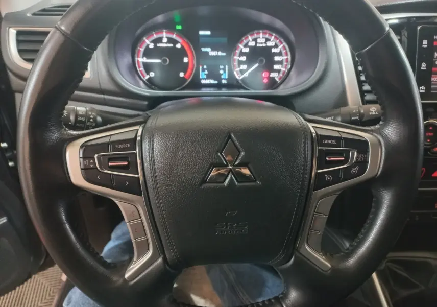 Vue rapprochée du volant cuir noir multifonctions du Mitsubishi L200 2020 avec tableau de bord et compteurs éclairés.