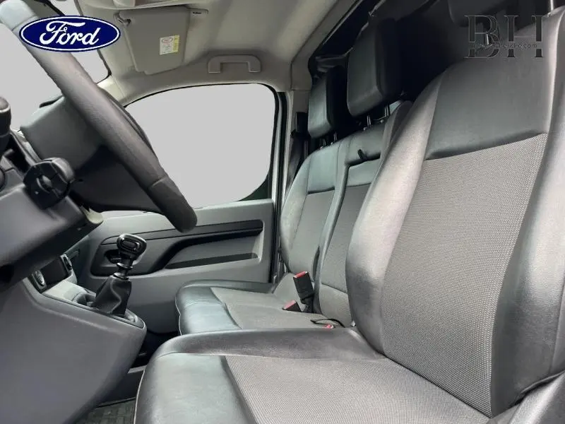 Vue intérieure côté conducteur du Citroën Jumpy blanc Banquise, montrant la banquette avant Moduwork et le levier de vitesse manuel.