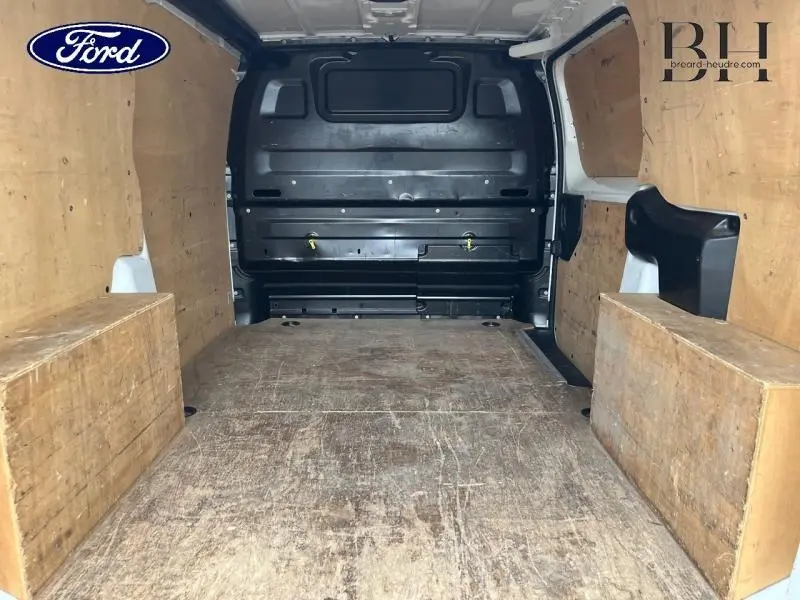 Vue intérieure arrière d'un utilitaire blanc avec aménagements en bois sur les parois et le sol, sans chargement visible.