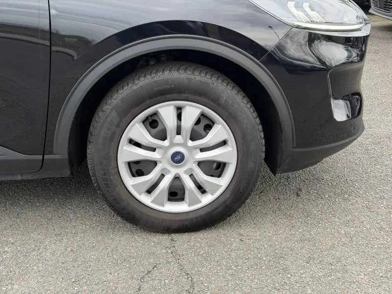 Gros plan sur la roue avant gauche d'un Ford Kuga 2024 noir, avec jante argentée et logo Ford au centre.