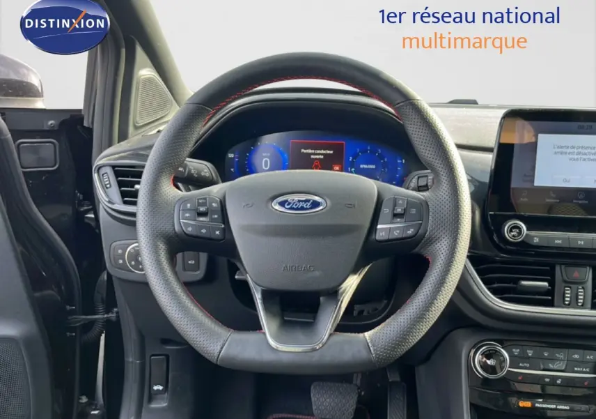 Vue intérieure centrée sur le volant perforé noir avec coutures rouges du Ford Puma 2023, tableau de bord et écran tactile visibles.