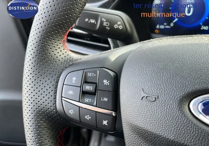 Gros plan sur le volant noir perforé avec surpiqûres rouges du Ford Puma 2023, boutons de commande visibles côté gauche.