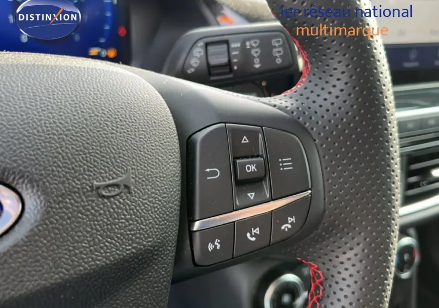 Gros plan sur le volant perforé avec surpiqûres rouges du Ford Puma noir Agate 2023, montrant les commandes multifonctions.