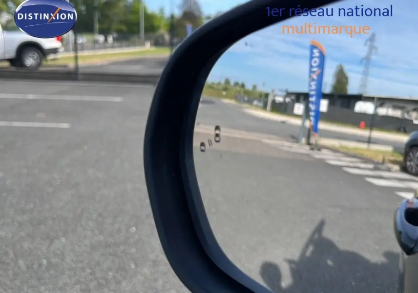 Rétroviseur côté droit d'un Ford Puma noir agate métal 2023, avec reflet d'une route et d'un drapeau Distinxion.