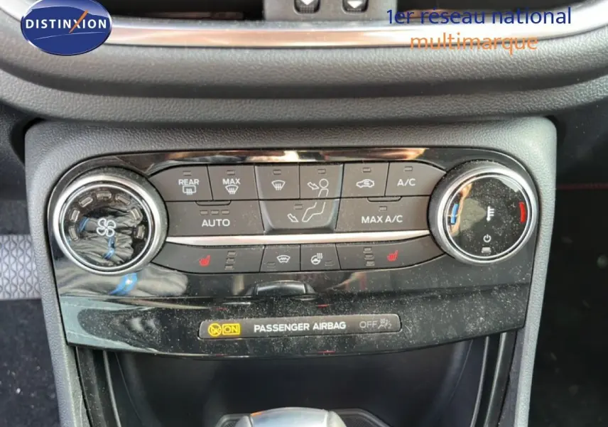 Gros plan sur la console centrale de la Ford Puma noire, montrant les commandes de climatisation et le témoin d’airbag passager.