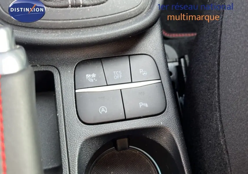 Gros plan sur les commandes centrales et porte-gobelet d’un Ford Puma noir agate métal, intérieur tissu noir avec surpiqûres rouges.