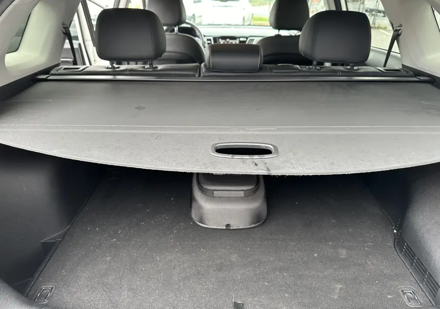 Vue du coffre avec cache-bagages déployé et sièges arrière noirs d'un KIA NIRO hybride rechargeable blanc céleste de 2020.