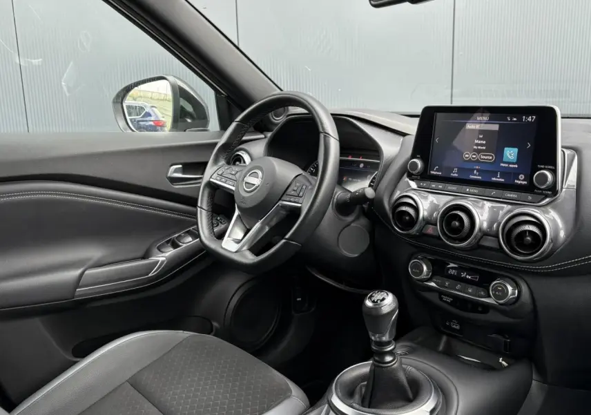 Intérieur du Nissan Juke 2023 vu côté conducteur, volant cuir, écran tactile et levier de vitesse manuel visibles.