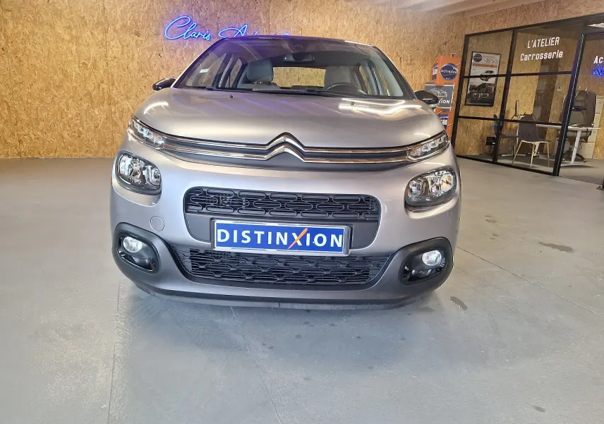 Vue frontale d'une Citroën C3 gris métallisé 2019 avec calandre noire et phares distinctifs en intérieur d'atelier.