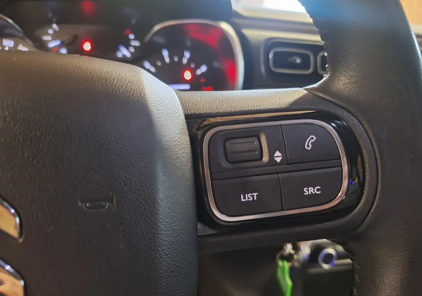 Gros plan sur les commandes du volant cuir de la Citroën C3 gris 2019, avec tableau de bord éclairé en arrière-plan.