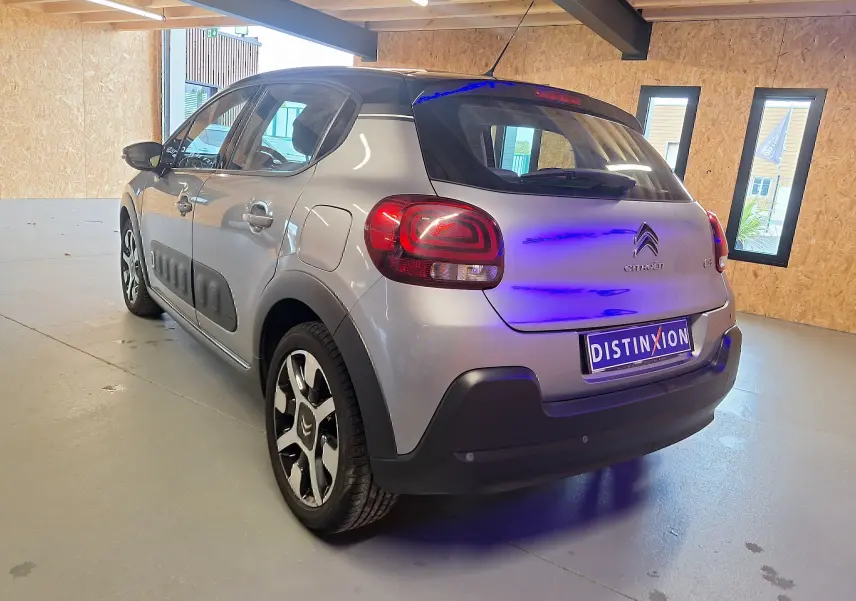 Vue 3/4 arrière droite d'une Citroën C3 gris avec toit noir et protections latérales noires en intérieur showroom.