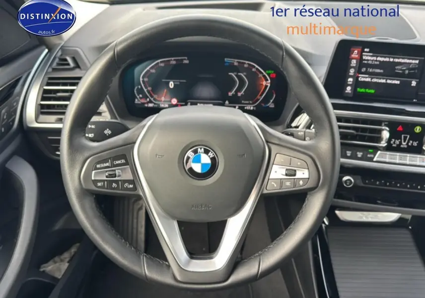 Vue centrée sur le volant cuir multifonction d'une BMW X3 2024, tableau de bord numérique et écran tactile visibles.
