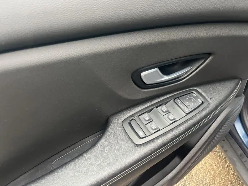 Gros plan sur la porte côté gauche du Renault Grand Scenic 2022 bleu Cosmos, montrant les commandes des vitres et la poignée intérieure.