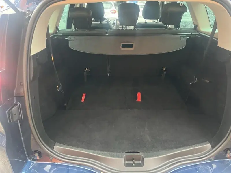 Coffre ouvert vu de l'arrière d'un Renault Grand Scenic bleu Cosmos, montrant la tablette cache-bagages et sièges arrière.