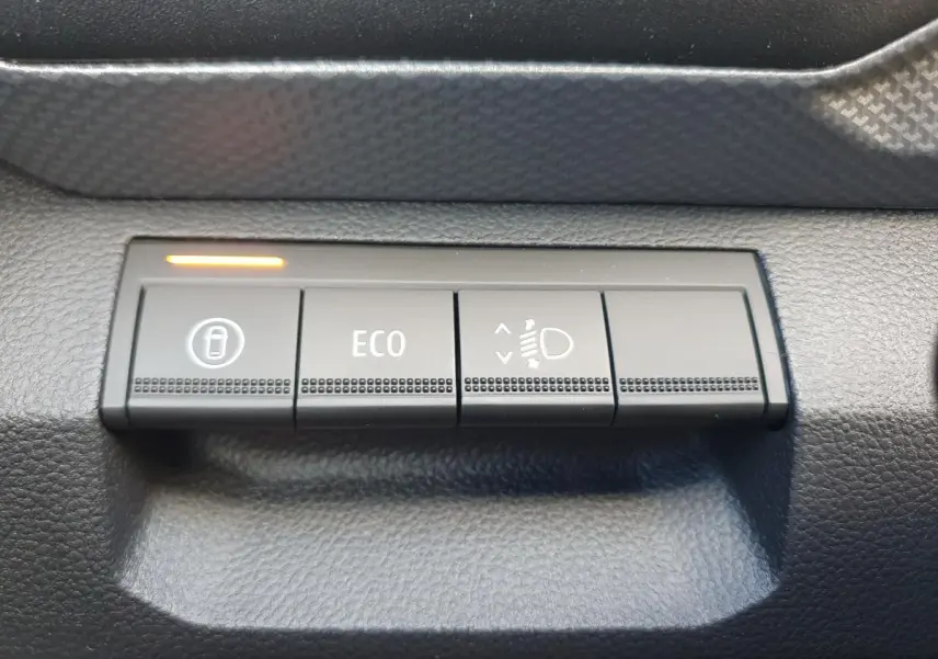 Boutons de commande du tableau de bord du Dacia Duster 2026, vue rapprochée sur les fonctions verrouillage, mode ECO et réglage des phares.