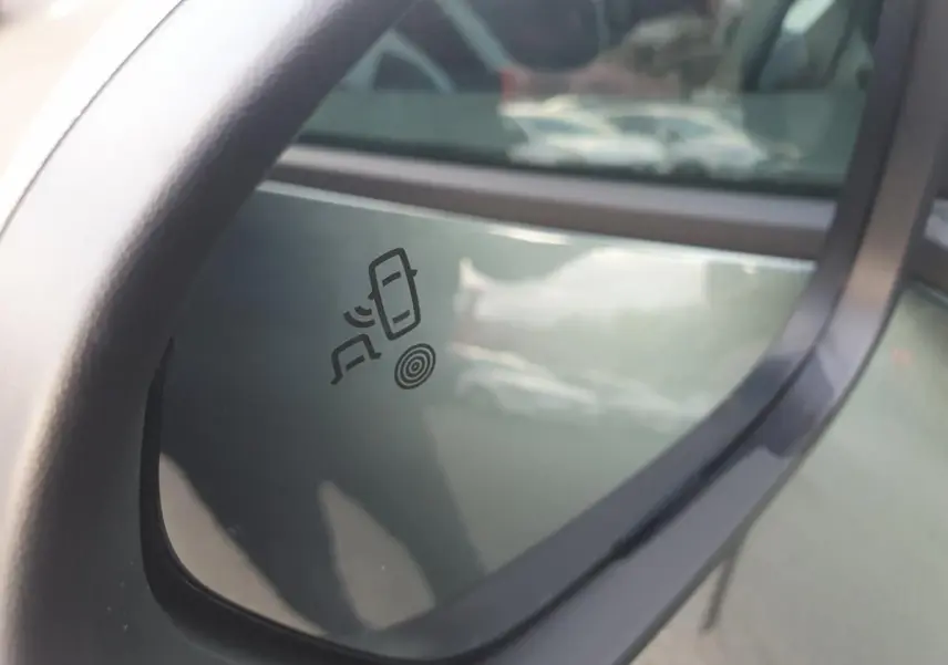 Rétroviseur extérieur gauche du Dacia Duster vert cèdre 2026 avec symbole d'alerte d'angle mort visible.